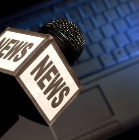 The word News on the side of a broadcast microphone with computer keyboard laptop background for download or podcast or online news concept. Loads of copy space.