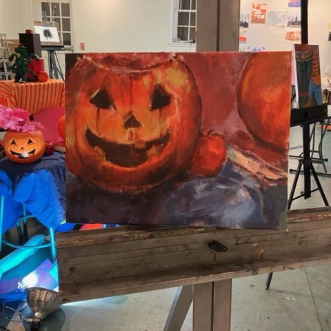 A painting of a pumpkin sits on an easel in an art class.
