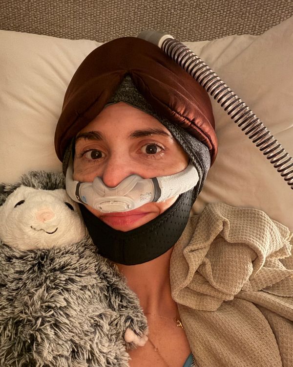 A photo of a woman in a CPAP mask, wearing a sleep mask, and holding a stuffed animal.