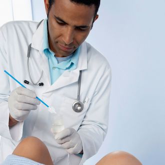 MODEL RELEASED. Doctor obtaining a cervical smear. He is holding a plastic spatula over a jar of water that will be used to lubricate the spatula. He will insert the spatula into the woman's vagina to scrape a specimen of cellular material from the neck (cervix) of the uterus. The extracted specimen of cells is then smeared onto a slide and examined in a laboratory. This procedure is also known as a pap test. Cells that appear abnormal may indicate developing cervical disease or cancer. This is a modern, brush-like plastic spatula. Traditionally, wooden spatulas were used to obtain cervical smears.