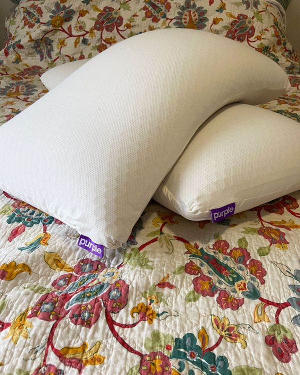 Two Purple Harmony pillows stacked criss-cross on top of one another on a bed.