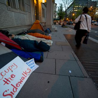 Members of Occupy DC sleep on a city sidewalk as pedestrians pass by March 26, 2012 in Washnigton, DC. The Occupiers are no longer allowed to sleep in McPherson Square, although they still maintain symbolic empty tents. AFP PHOTO/Karen BLEIER (Photo credit should read KAREN BLEIER/AFP/Getty Images)