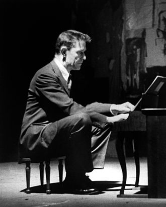 Avant-garde minimalist composer John Cage playing a children's size piano. 