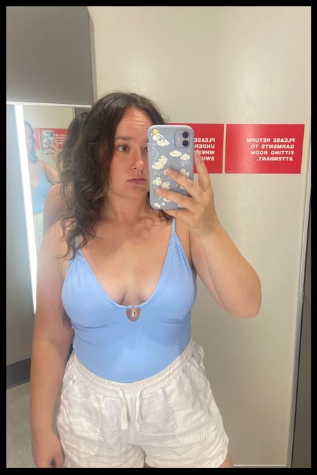 A person in a blue one piece swimsuit in a dressing room.