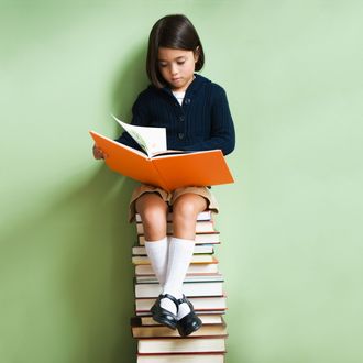 Mixed race girl sitting on stack of books reading book --- Image by ? KidStock/Blend Images/Corbis