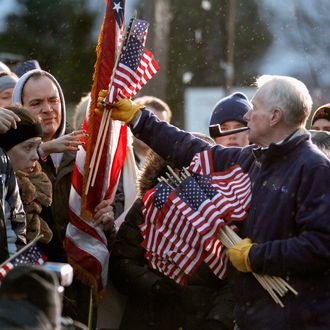 WEST DES MOINES, IA - DECEMBER 30: As a light and steady rain falls, Jim Wilson of Buckingham, Virginia, hand out United States flags to supporters before the start of a campaign rally with former Massachusetts Governor and Republican presidential candidate Mitt Romney at a Hy Vee supermarket December 30, 2011 in West Des Moines, Iowa. Despite cold wind and rain, hundreds of Romney supporters came out to see the candidate just days before the 