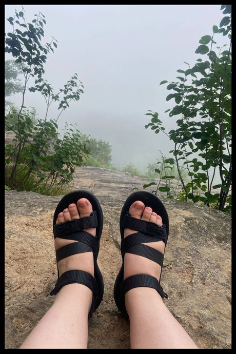 A photo of a person's feet, wearing black sandals, on a foggy mountain.
