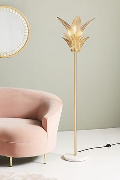 A gold metallic Palm Frond Floor Lamp from Anthropology with an upward facing palm-frond lamp shade and a round white marble base The lamp is shown with a round mirror, grey walls, and a pink sofa. The Strategist - 33 Things on Sale You’ll Actually Want to Buy: From Adidas to Le Creuset