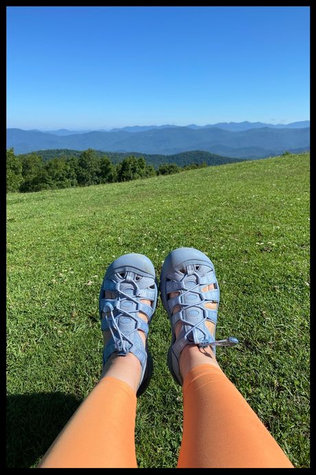 A photo of a person's feet, wearing blue covered-toe sandals, on top of a mountain.