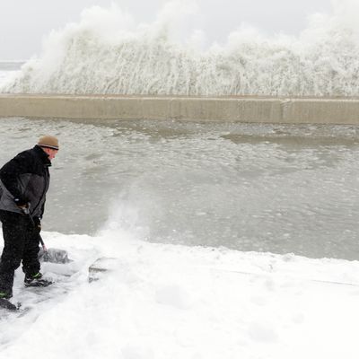 WINTHROP, MA - FEBRUARY 09: Mike Streeter shovels snow in his front yard as ocean water crashes over the sea wall just feet away on February 9, 2013 in Winthrop, Massachusetts. The powerful storm has knocked out power to 650,000 and dumped more than two feet of snow in parts of New England. (Photo by Darren McCollester/Getty Images)