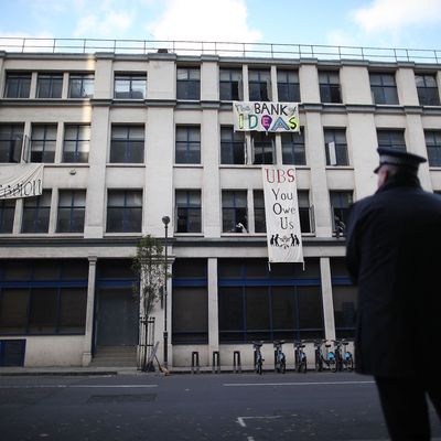 LONDON, ENGLAND - NOVEMBER 18: A policeman watches as Occupy London protestors hang banners from an unused building owned by UBS bank on November 18, 2011 in London, England. The Occupy London protest group are continuing to camp outside St Paul's Cathedral and nearby Finsbury Square in the heart of London's financial district. The deadline for those outside the cathedral to leave or face court action has passed. (Photo by Peter Macdiarmid/Getty Images)