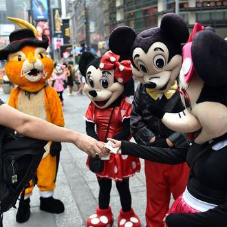 A tourist (L) tips a Minnie Mouse character after he posed for a photograph with the cartoon figures July 28, 2014 in New York's Times Square. The panhandler characters pose for tourists and work for tips, which can sometimes lead to disputes, like the Spider-Man character arrested on July 26, for assaulting a police officer after an argument with a tourist over the amount of the tip. AFP PHOTO/Stan HONDA (Photo credit should read STAN HONDA/AFP/Getty Images)