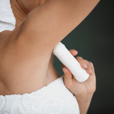 Young lady wrapped in white towel apply antiperspirant in armpit