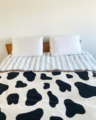 A bed with a striped comforter and a cow-spot pattern blanket whose four pillows are covered in silk pillowcases.