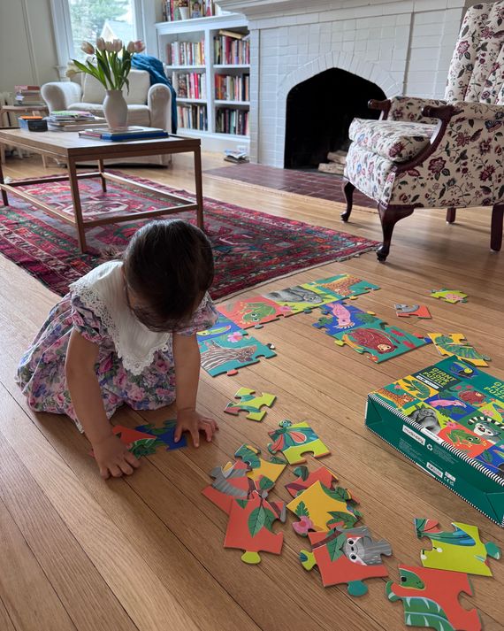 A young child putting together a jigsaw puzzle on the floor of a living room.