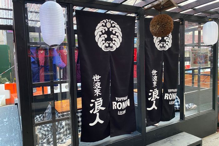 A wooden outdoor dining structure with two black blankets as doors that read 