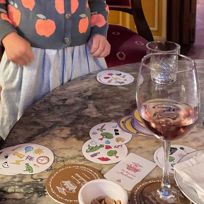 Two kids playing the card game Spot It at a restaurant table strewn with silverware and wine glasses.