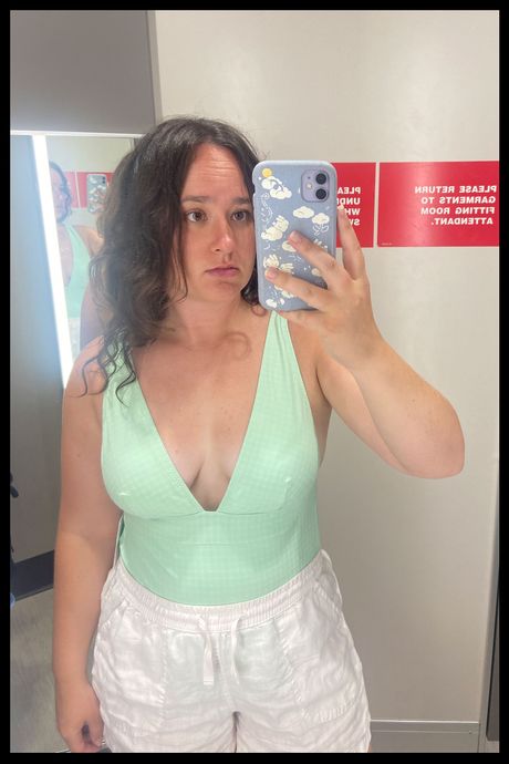 A person in a green one piece swimsuit in a dressing room.
