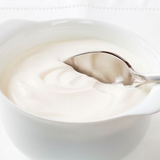 A bowl of Greek yoghurt with a spoon, white on white.