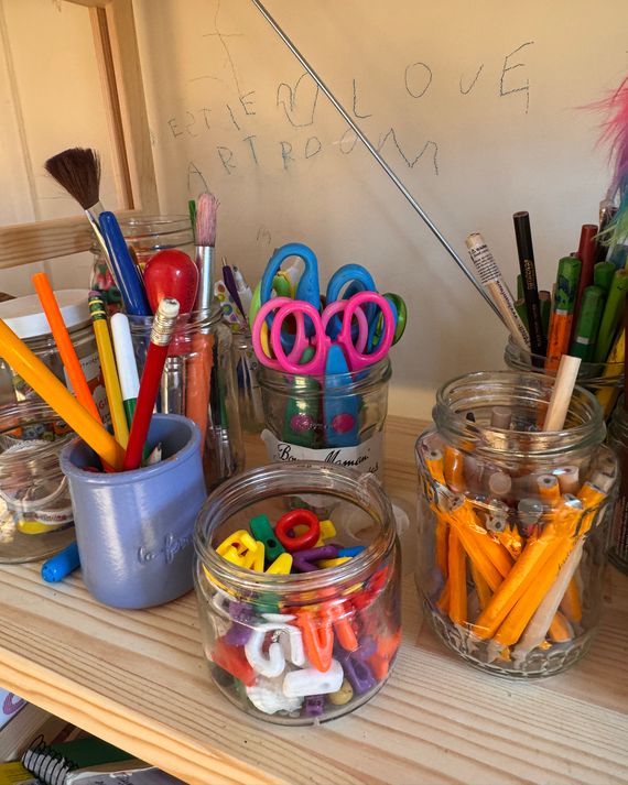 A shelf with jars of scissors, golf pencils, beads, and other art supplies.