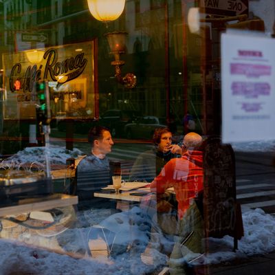 Several people sitting inside Caffe Roma as seen through the street window.
