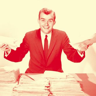 Amused smiling businessman holding papers from the piles on his desk.