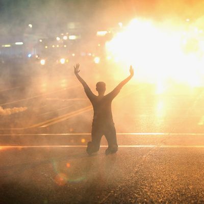 FERGUSON, MO - AUGUST 17: Tear gas reigns down on a woman kneeling in the street with her hands in the air after a demonstration over the killing of teenager Michael Brown by a Ferguson police officer on August 17, 2014 in Ferguson, Missouri. Despite the Brown family's continued call for peaceful demonstrations, violent protests have erupted nearly every night in Ferguson since his August 9, death. (Photo by Scott Olson/Getty Images)