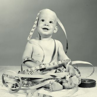 01 Jun 1964 --- 1960s smiling seated baby wrapped up in tangled tape measure --- Image by ? ClassicStock/Corbis