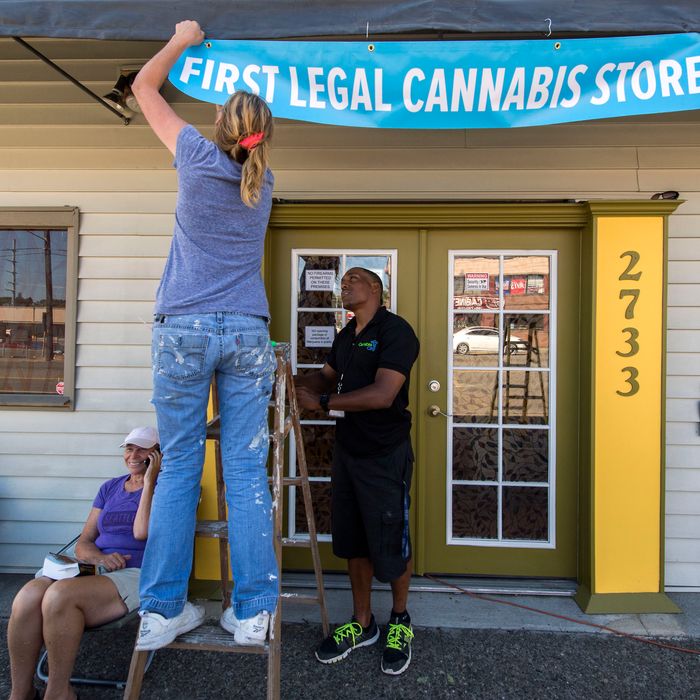 July 7, 2014 - Seattle, Washington, U.S. - ANDREW POWERS helps WENDY COOK put up a banner at Cannabis City, the sole dispensary in Seattle with a state license to sell recreational marijuana to the public on July 8, 2014, the first day of legal sales in the state of Washington. Seated at left are the first two persons to secure a place in line, DEB GREENE and GEORGE VARGAS. (Credit Image: ? Brian Cahn/ZUMA Wire)