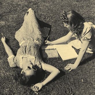 Two teenage girls (14-16) on grass, one doing homework (B&W)