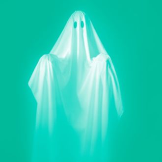 CIRCA 1960s: Person Wearing A Ghost Costume, Made Out Of A White Sheet With Two Holes In It. Highlights Are On The Sheet, The Background Is Pitch Black.