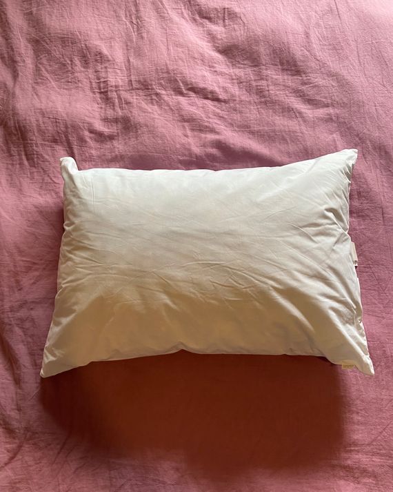 A white pillow on a pink duvet.