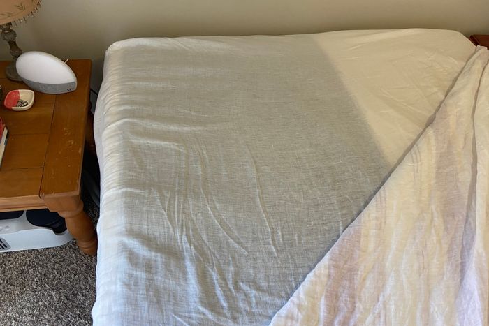 A mattress with a white, sheer fitted sheet on top. The dark gray Chilipad is visible through the sheet.