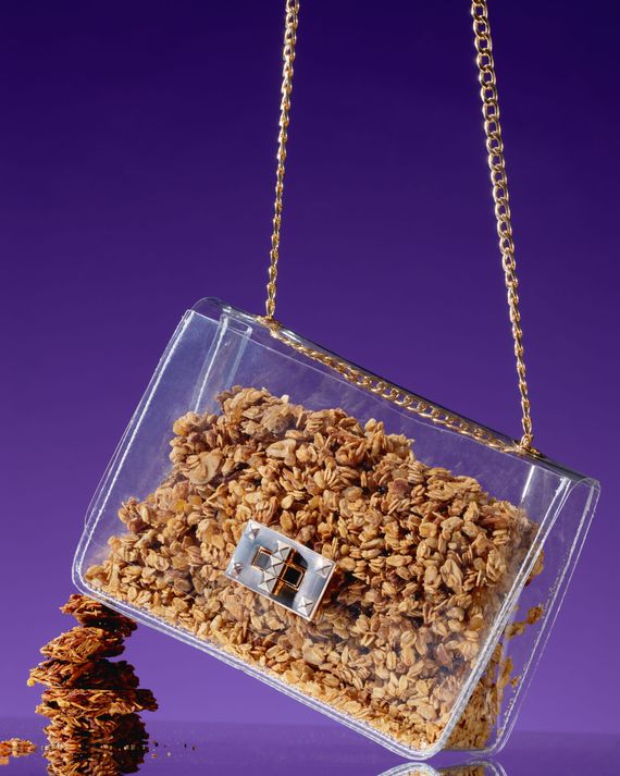 A clear purse on a gold chain filled with granola against a purple background.