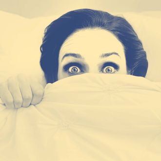 A young woman peeking out from under her ned sheet with a frightened expression.