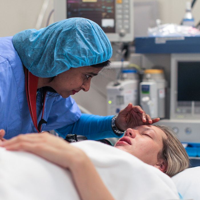 A doula supports and comforts her emotional pregnant client as she lays in the operating theatre during a caesarean section.