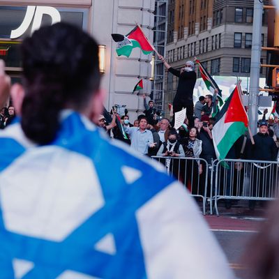 A protester wearing an Israeli flag as a cape faces a crowd of counterprotesters waving Palestinian flags.