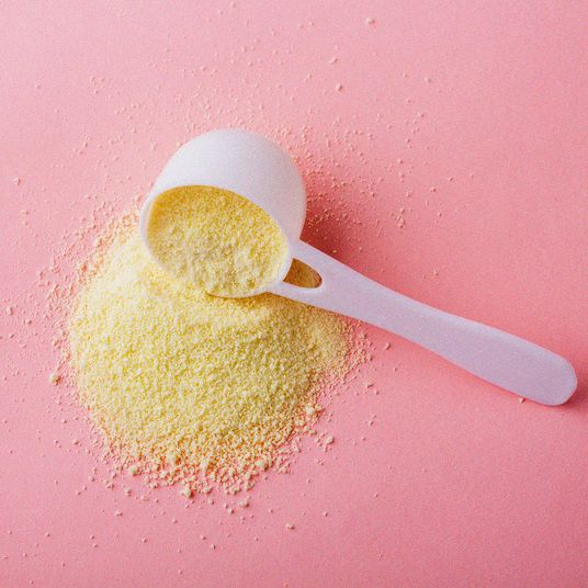 Powdered milk in plastic spoon on pink background