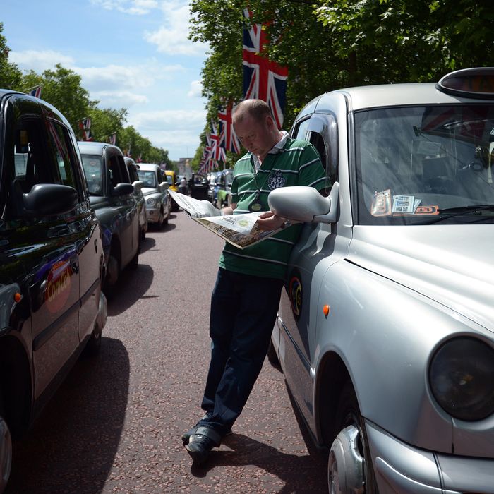 A London black cab driver reads a newspaper during a protest against a new private taxi service 'Uber', a mobile phone app, on the Mall leading to Buckingham Palace in central London on June 11, 2014. Taxi drivers brought parts of London, Paris and other European cities to a standstill on June 11 as they protested against new private cab apps such as Uber which have shaken up the industry. Thousands of London's iconic black cabs, many of them beeping their horns, filled the roads around Buckingham Palace, Trafalgar Square and the Houses of Parliament to the exclusion of any other vehicles. AFP PHOTO / CARL COURT