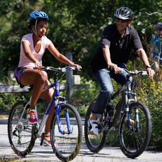 WEST TISBURY, MA - AUGUST 23: U.S. President Barack Obama (R) and daughter Malia Obama, 13, bike together on a bike path through Manuel F. Correllus State Forest while vacationing on Martha's Vineyard on August 23, 2011 in West Tisbury, Massachusetts. This is the third year the president has taken his vacation on Martha's Vineyard. (Photo by Matthew Healey-Pool/Getty Images)