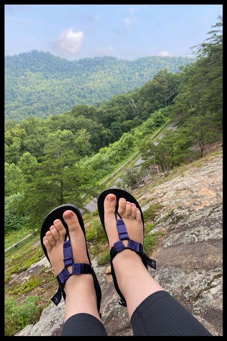 A photo of a person's feet wearing purple and black sandals at a mountain overlook.