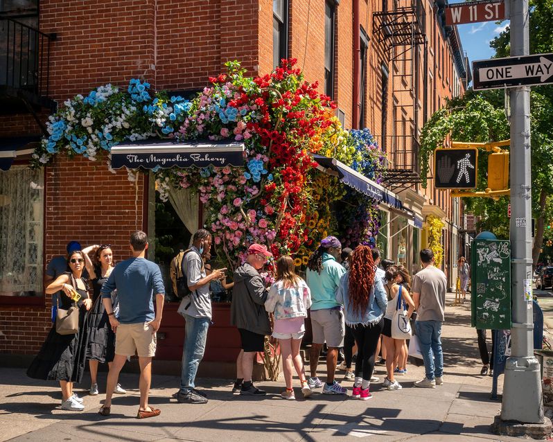 Customers queue up outside the Magnolia Bakery in Greenwich Village in New York on Sunday June 19, 2022, decorated with a faux floral display. (© Richard B. Levine)