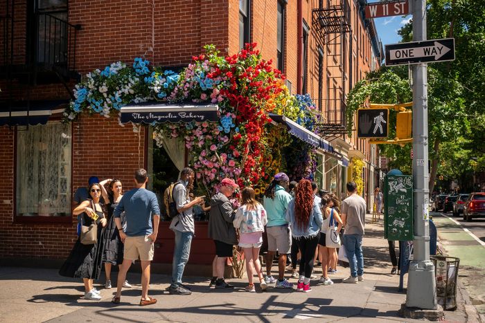 Customers queue up outside the Magnolia Bakery in Greenwich Village in New York on Sunday June 19, 2022, decorated with a faux floral display. (© Richard B. Levine)