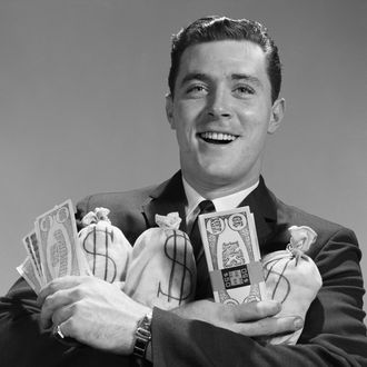 Smiling man holding money bags and bundles of cash 