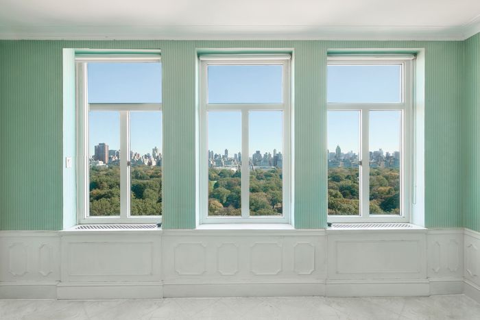 A room with three windows overlooking trees and skyline with tall buildings.