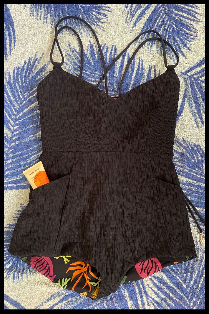 A swim romper laying flat on a beach towel with a tube of sunscreen sticking out of one of the pockets.