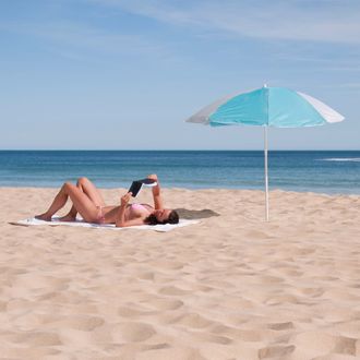 Portugal, Lagos, Mid adult woman reading book on beach