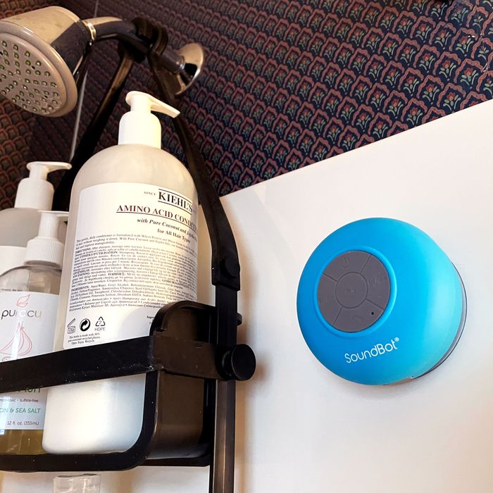 The SoundBot shower speaker suctioned to the wall of a shower, next to a shower caddy.