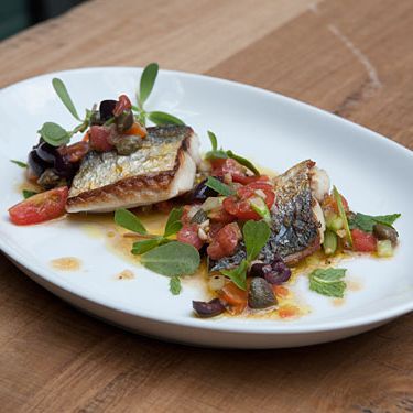 西班牙鲭鱼在铁板上烹饪，配上新鲜的puttenesca风格的酱汁，配上市场上的番茄，刺山柑，盖塔橄榄，新鲜薄荷和蒜花。完成了马齿苋。