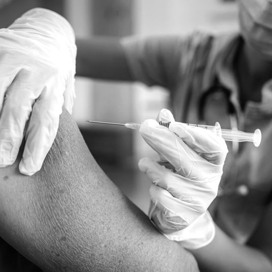 Closeup of nurse with protective face mask on sitting at home and giving injection to an old woman during corona outbreak.
